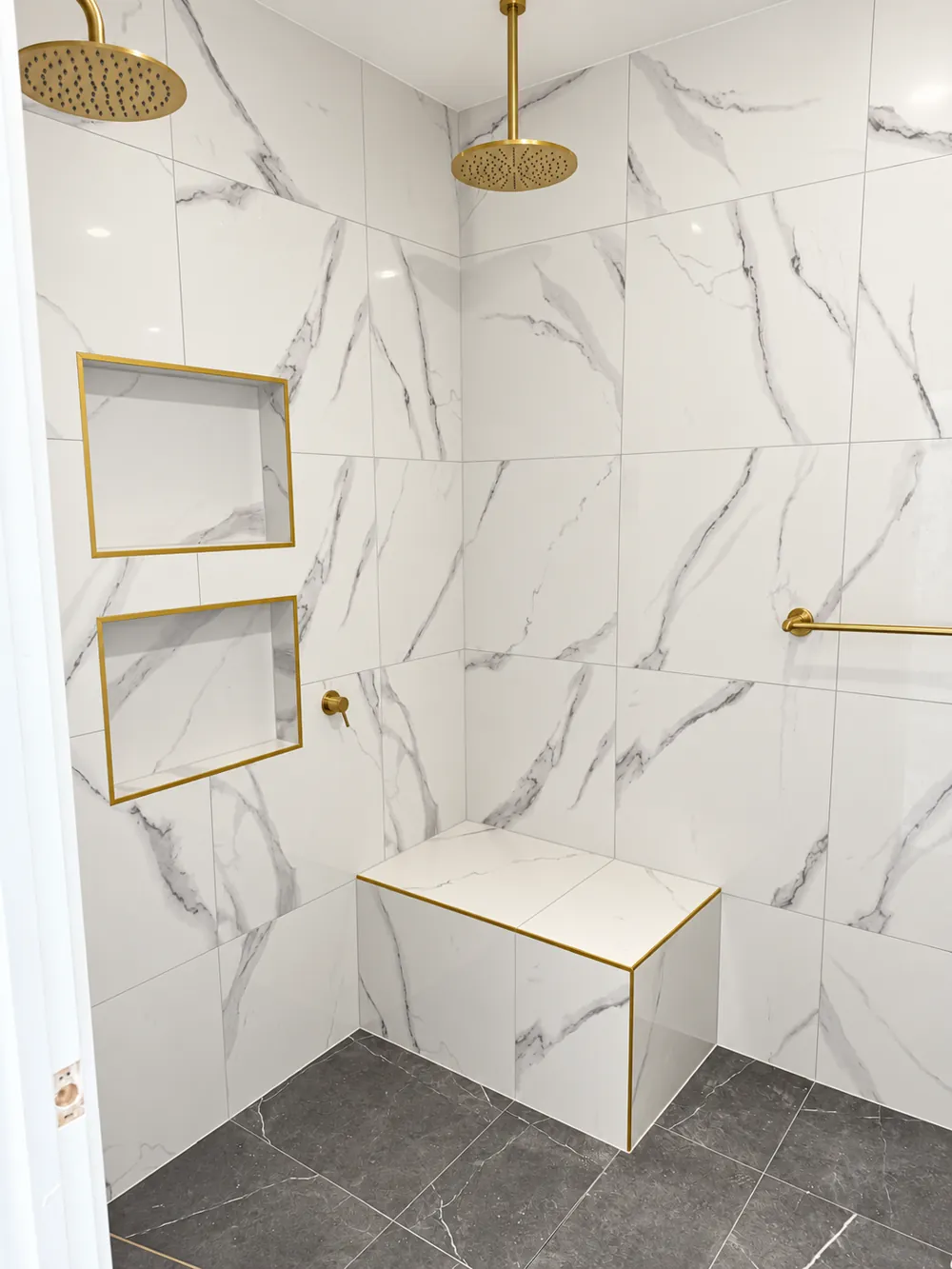Marble-look shower with brass rainfall showerhead, brass-trimmed niches and built-in bench