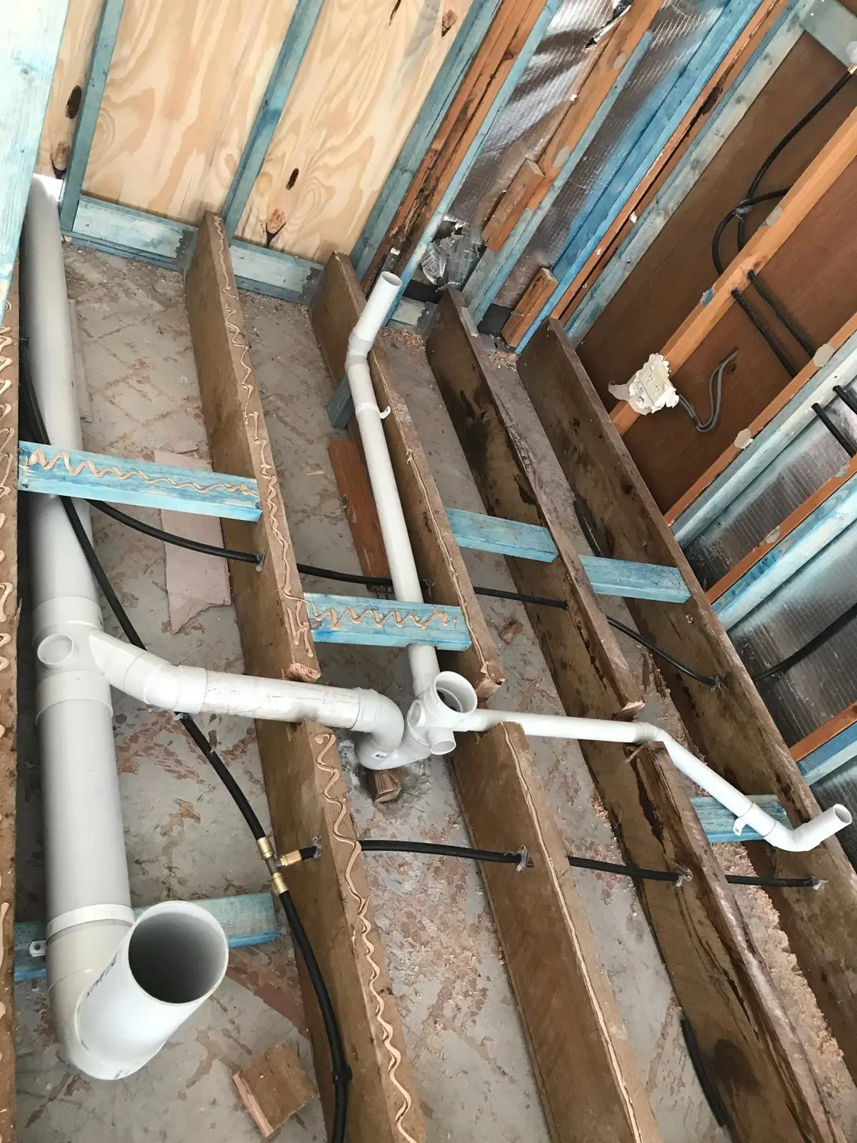 Bathroom subfloor with exposed floor joists and new plumbing rough-in pipework