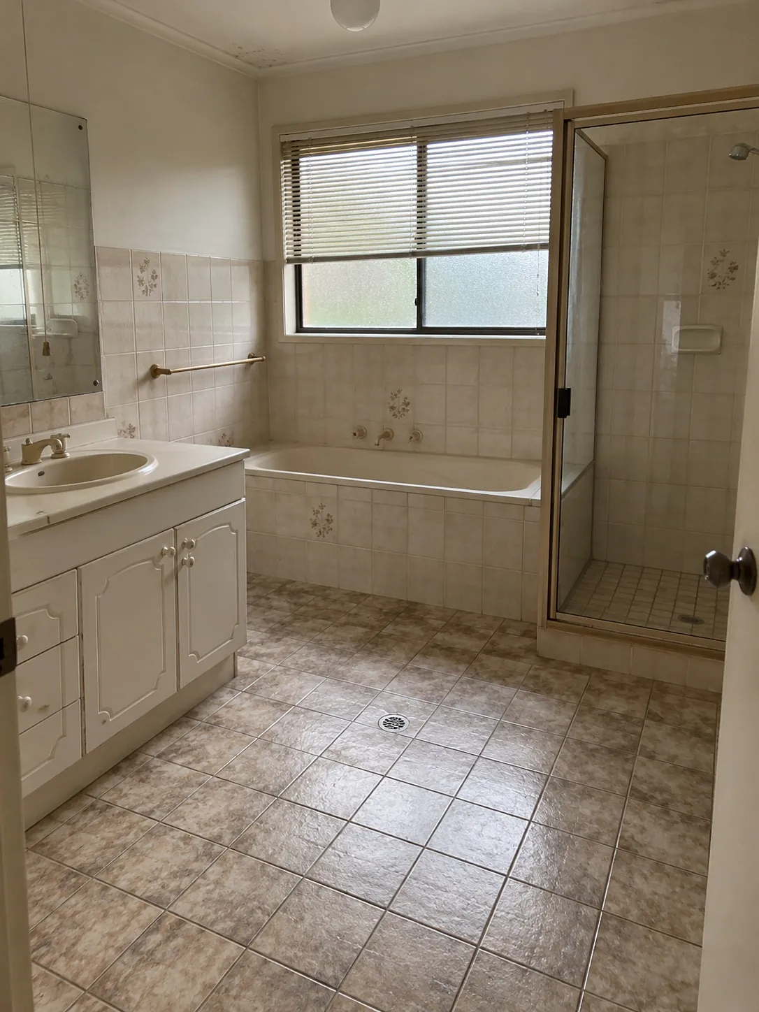 Original bathroom before renovation, with cream wall tiles, a tiled bathtub, a framed glass shower and beige stone-look floor tiles